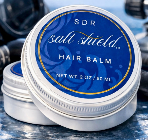 Two 2 oz tins of Salt Shield Pre-Dive Hair Balm with blue labels beside scuba gear